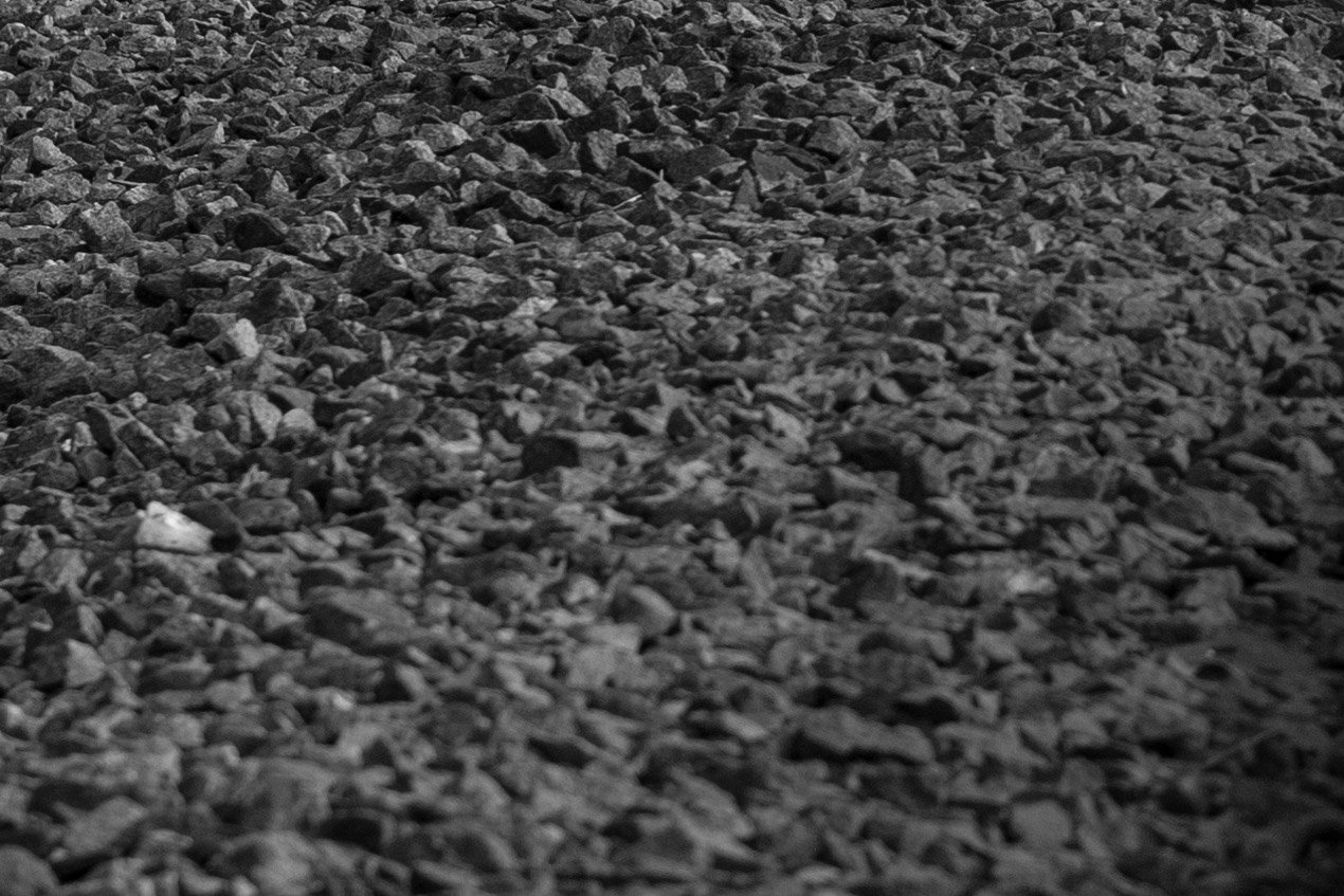 A close-up view of a rough surface covered with small, uneven, dark-colored stones or gravel, creating a textured and rugged pattern.