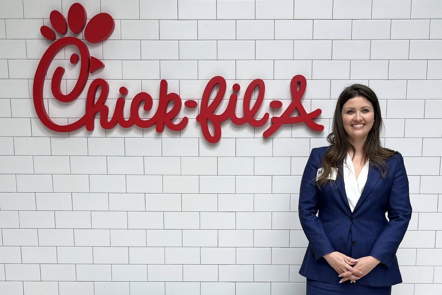 Sophia R. Holley stands smiling in front of a white tiled wall with a red Chick-fil-A logo.